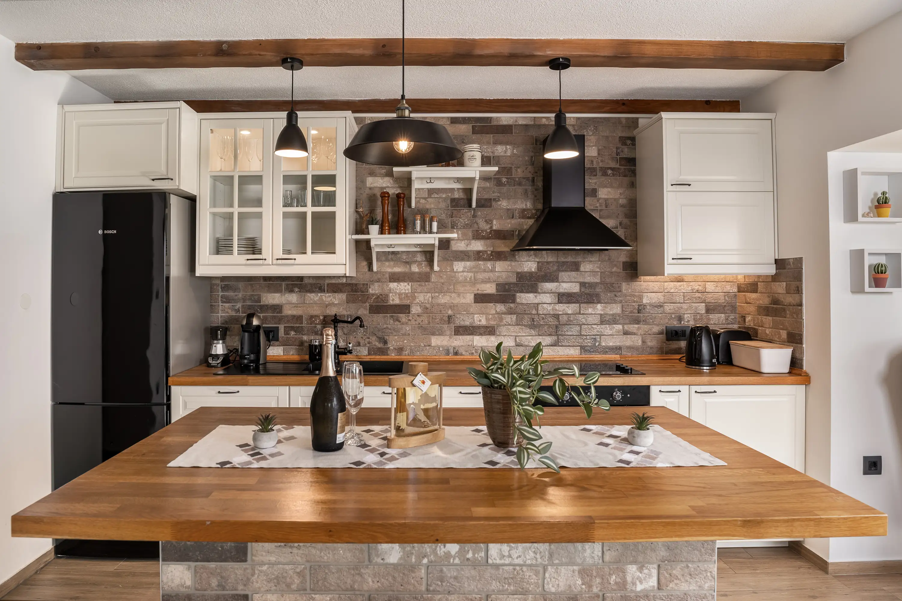 Kuhinja s ciglenom pozadinom, drvenim radnim pločama, industrijskim svjetiljkama i otokom