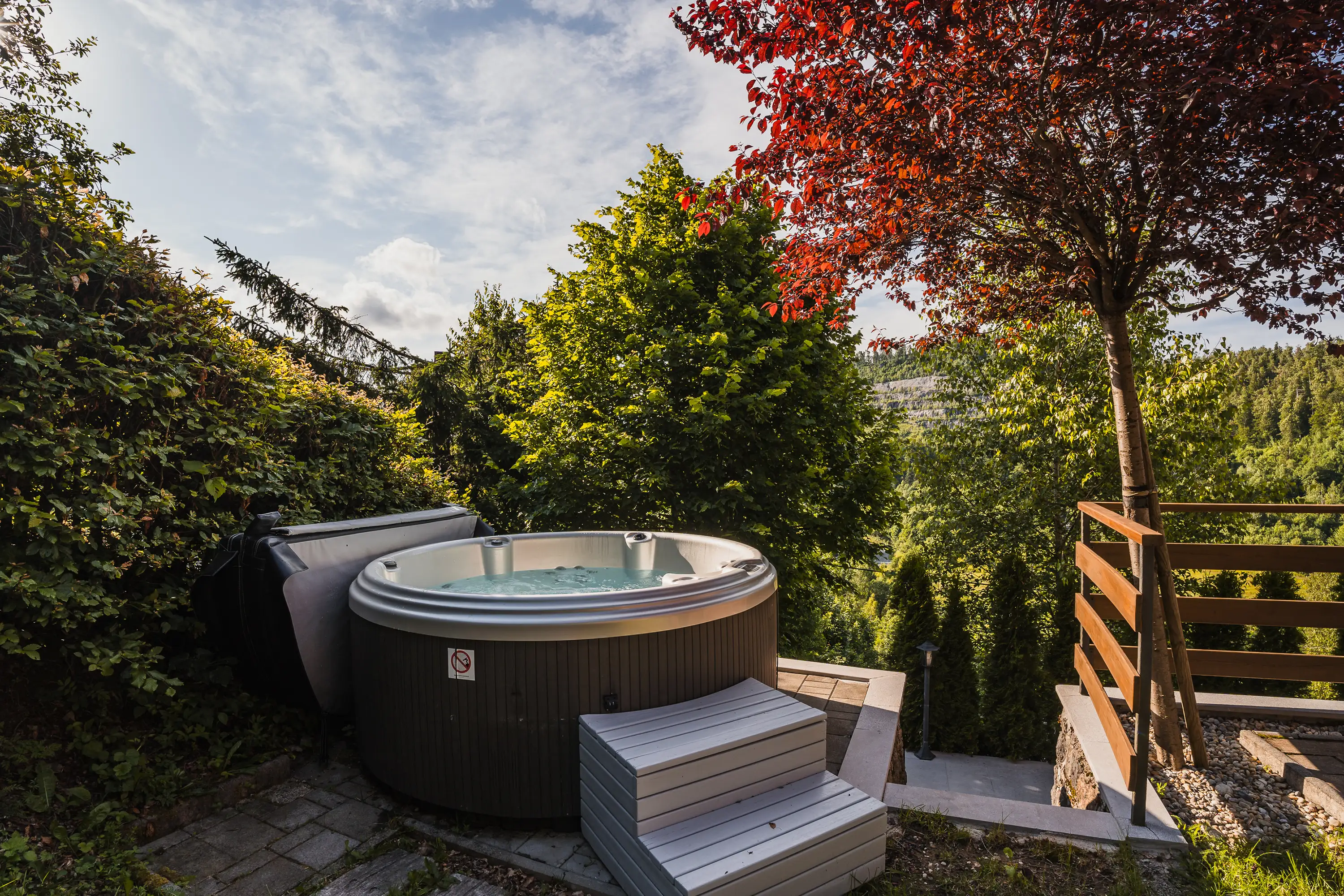 Jacuzzi na otvorenom okružen bujnim zelenilom s jesenskim drvetom i pogledom na brežuljak