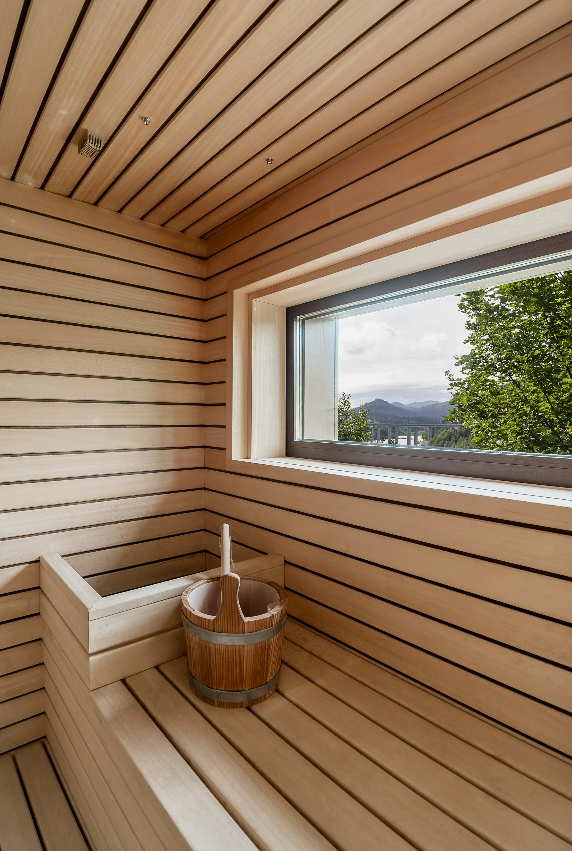 Unutrašnjost drvene saune s panoramskim prozorom i pogledom na planine