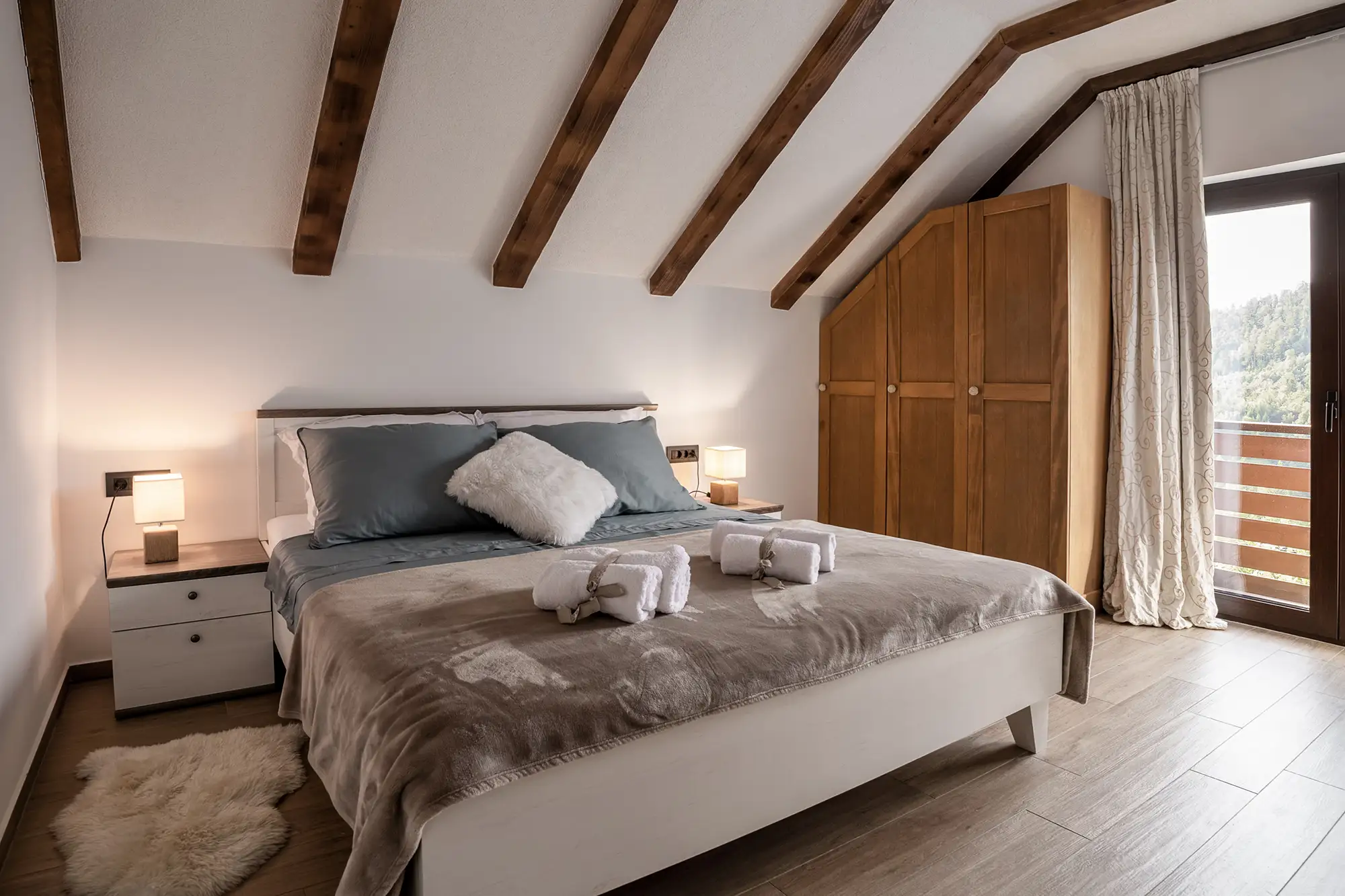 Potkrovna spavaća soba sa sivo-plavom posteljinom, drvenim ormarom i pogledom na planine